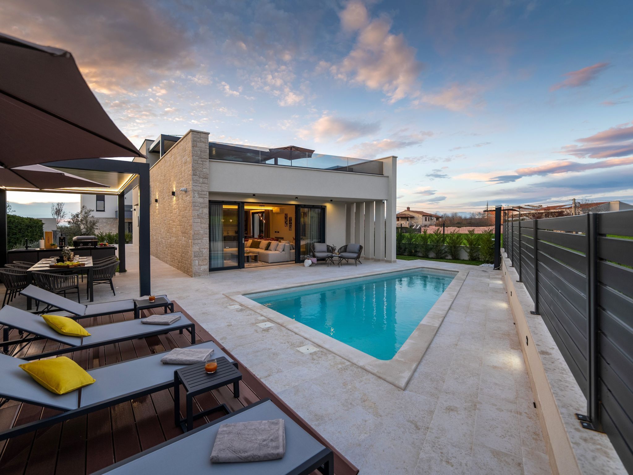 A modern outdoor pool area with a built-in barbecue, lounge chairs, and a view of the cityscape.
