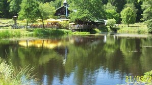 Rauhallinen paikka järven rannalla, jossa on puinen mökki ja veden äärellä sijaitseva huvimaja.