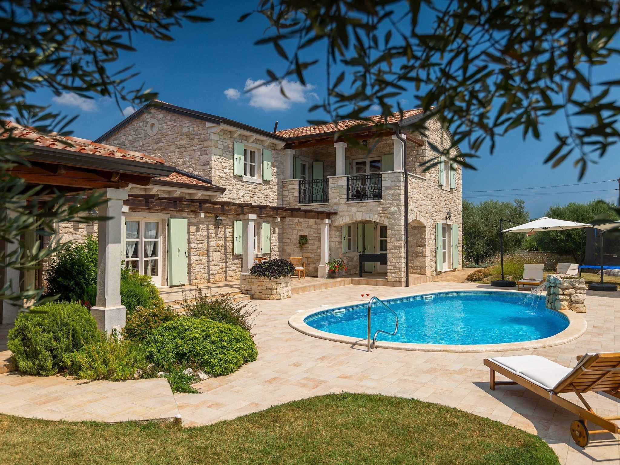 A two-story stone house with a swimming pool, outdoor seating, and a well-maintained garden.