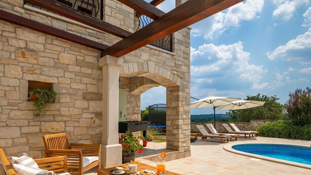 Une terrasse en pierre avec des meubles d’extérieur, une piscine et une vue sur le paysage.