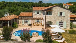 Une maison en pierre à deux étages, dotée d’une piscine, d’un espace salon extérieur et offrant une vue sur la forêt environnante.