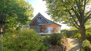 Een huis met een stenen pad dat naar de ingang leidt, omringd door weelderige begroeiing en bomen.