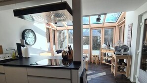 Een moderne keuken met een groot eiland, een klok en uitzicht op het exterieur door grote ramen.