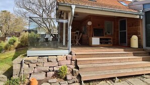 Een houten blokhut met een pannendak, een glazen uitbouw en een stenen muur.