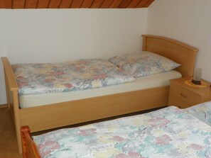 Een enkel bed met een bloemenprint sprei, een houten hoofdbord en een nachtkastje met een lamp.