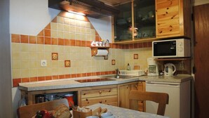 Une cuisine compacte avec un plan de travail carrelé, des placards en bois, un four à micro-ondes et un coin repas avec une table dressée pour deux personnes.