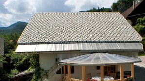 Un chalet doté d’un toit en pente et d’une terrasse en bois protégée par une paroi vitrée.