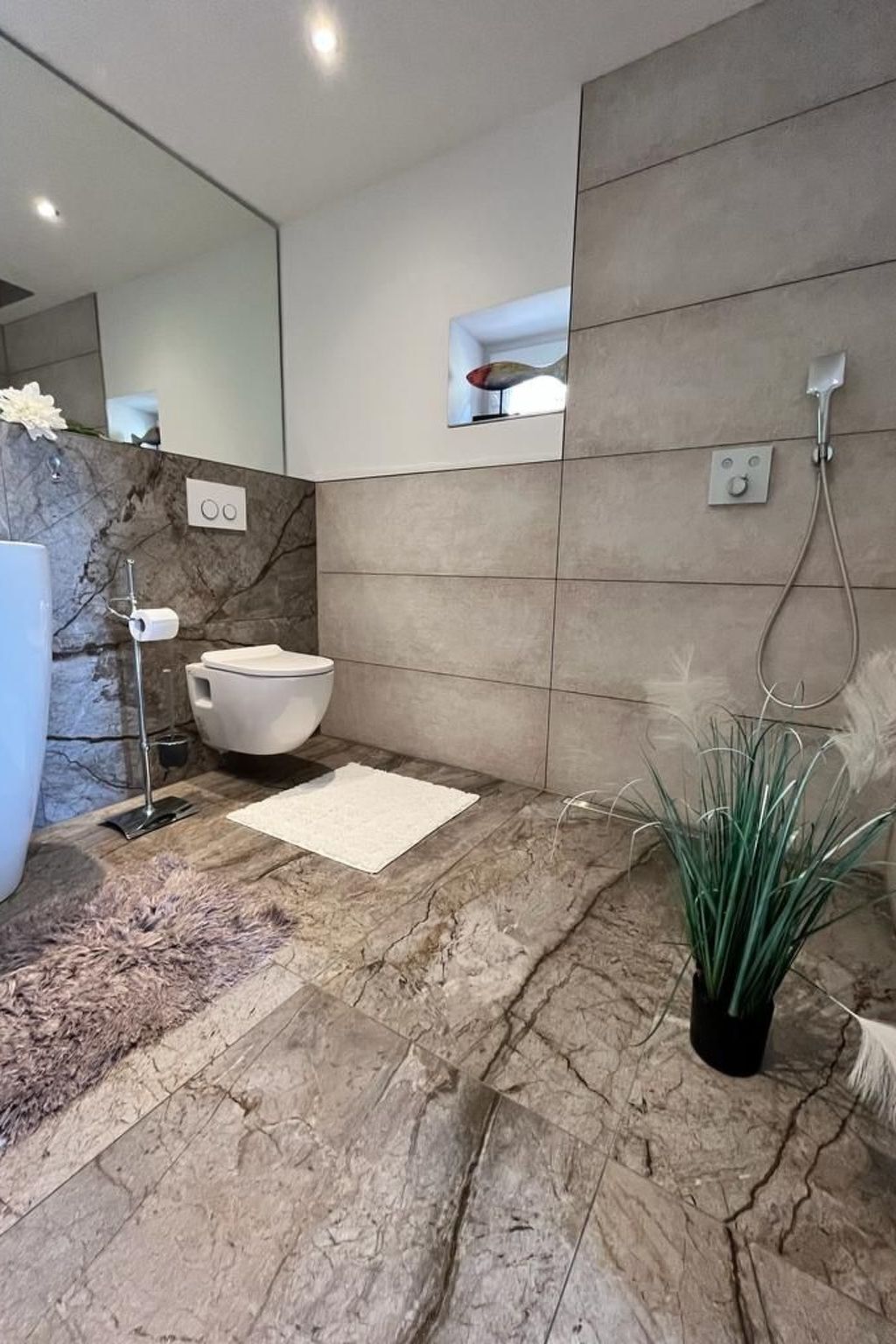 A modern bathroom with a marble floor, a white toilet, a sink with a mirror, and a shower with a control panel.