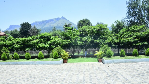 A paved courtyard with a landscaped garden, a mountain in the background, and a person standing in the distance. - Misty Green (Chikkamagaluru)