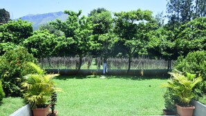 A patio with a view of a grassy area and trees, bordered by a low fence. - Misty Green (Chikkamagaluru)