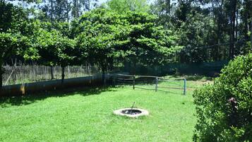 Un área cubierta de césped con un hogar circular, rodeado por una valla y árboles.