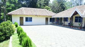 A building with a tiled roof, a covered patio area, and a garden with neatly trimmed bushes. - Misty Green (Chikkamagaluru)