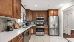 A modern kitchen with wooden cabinets, stainless steel appliances, a marble floor, and a white countertop. - The Stag House : HotTub, Outdoor Theatre, Arcade Games, Big Backyard & Sleeps 18 (Langley)