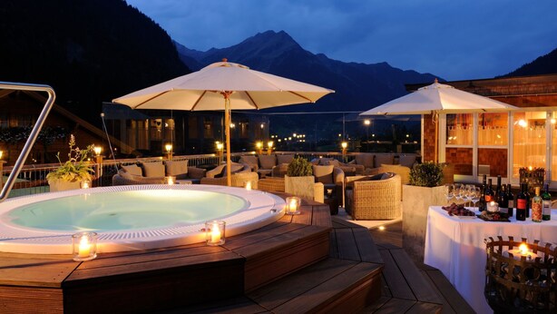 Un jacuzzi rodeado de asientos en terraza de madera, sombrillas exteriores y velas.