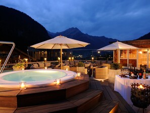 Un jacuzzi rodeado de asientos en terraza de madera, sombrillas exteriores y velas.