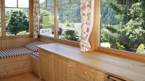 Una cabaña de madera con ventanas amplias, un banco y vistas a una zona montañosa boscosa.