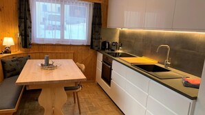 Una cocina compacta con una mesa y un banco de madera, horno integrado y lavamanos con grifo moderno.