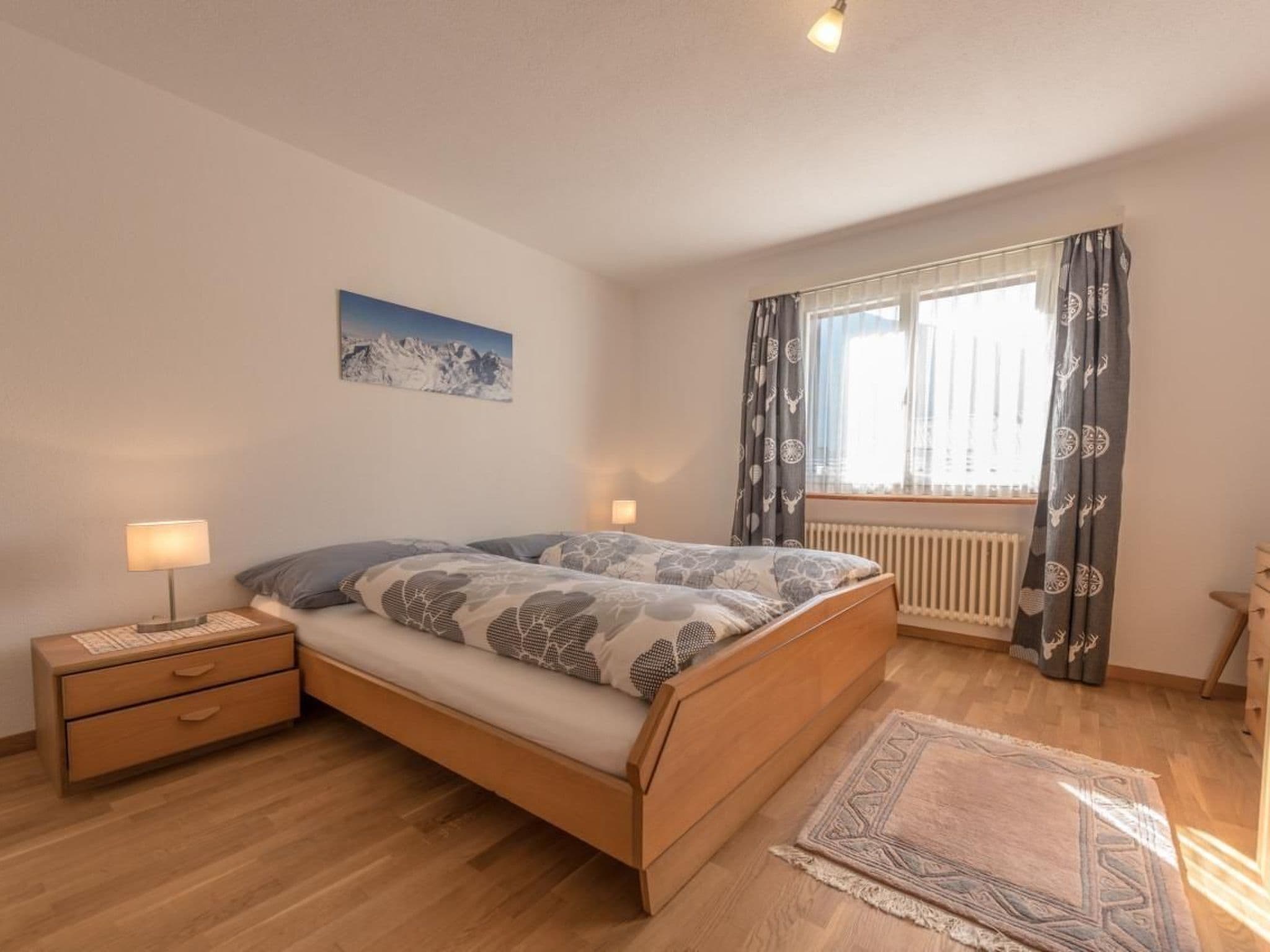 A bedroom with a wooden bed, a nightstand, a lamp, a window with curtains, and a radiator.