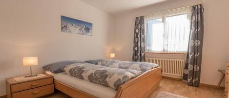A bedroom with a wooden bed, a nightstand, a lamp, a window with curtains, and a radiator.