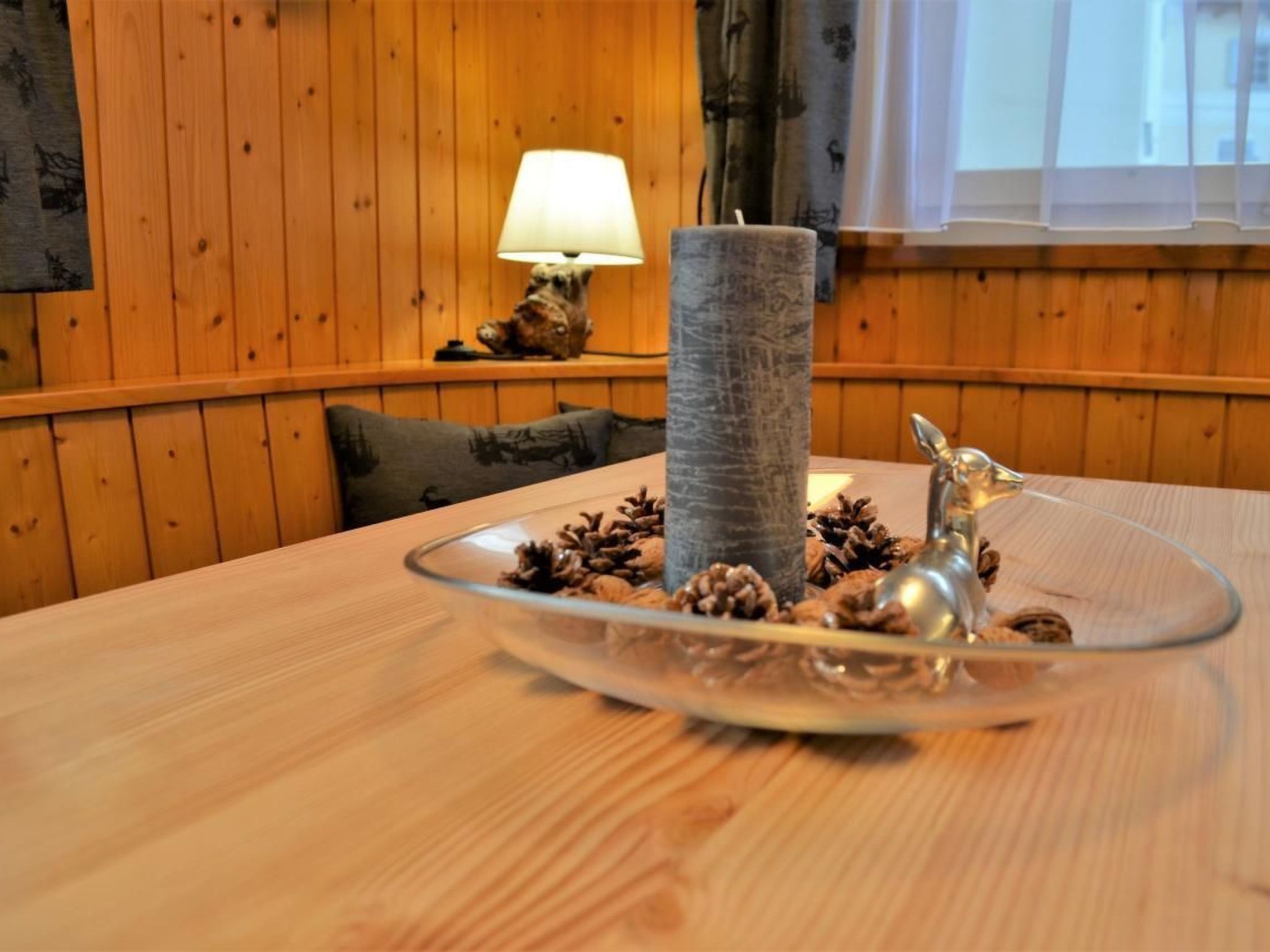 En inredning med trädetaljer och ett bord som har en glasdekoration i mitten, prydd med tallkottar och en silverfärgad djurfigur.