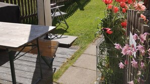 A patio with a table and chairs, a yellow umbrella, and a garden with red flowers. - Studio Chesa Marias by Interhome (Sils Maria)