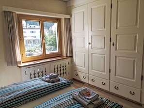 A bedroom with a window, a radiator, a bed with striped bedding, and a wardrobe. - 4 Bettwohnung by Interhome (Sils Maria)