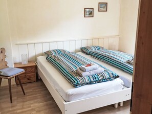 A bedroom with two beds, a wooden chair, a nightstand, and a wall-mounted shelf. - 4 Bettwohnung by Interhome (Sils Maria)
