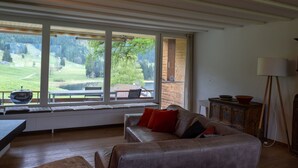 A living room with a large window, a sofa, a wooden cabinet, and a floor lamp.