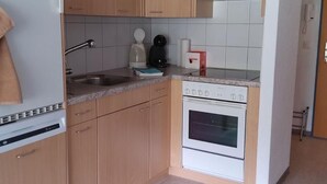 Eine kleine Küche mit Holzausstattung, einem weißen Kühlschrank, einem eingebauten Backofen und einer Arbeitsplatte mit Wasserkocher und Kaffeemaschine.