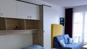 Ein Zimmer mit zwei Betten, jeweils mit blauer und gelber Bettwäsche. Darüber befinden sich Nachttische aus Holz und ein Fenster mit Vorhängen.