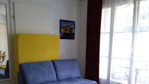 Ein Zimmer mit einem blauen Sofa, einem Holztisch und einem Vorhangfenster.