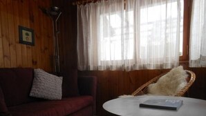 Una habitació acollidora amb un sofà vermell, una cadira de vugada i una taula rodona amb un llibre.