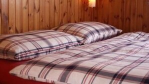 Una habitació amb parets revestides de fusta, un llit amb roba de llit escocesa i una làmpada fixada a la paret.