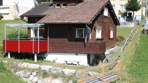 Una casa d'estil xalet amb façana de fusta, un balcó vermell i blanc, i fonaments de pedra.