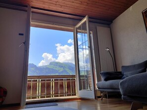 Ein Zimmer mit einer Schiebeglas-Tür, die auf einen Balkon führt, einem grauen Sofa und einer Holzzieldecke.