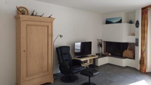 Una sala de estar con un aparador de madera, una silla negra, un televisor y una chimenea.