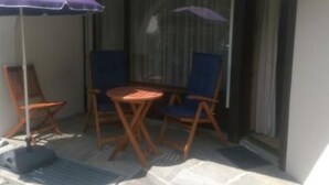 Un balcón con dos sillas de madera y una mesa pequeña, cubierto por un paraguas púrpura.