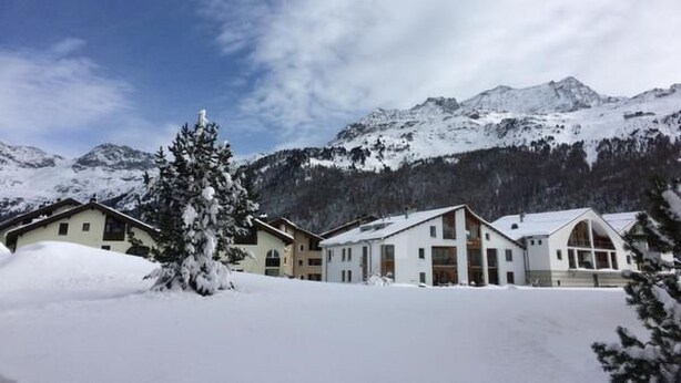 Un paisaje nevado de montañas con una hilera de edificios modernos al frente, probablemente un hotel.