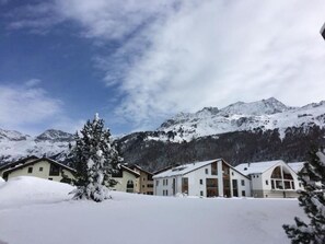Eine verschneite Berglandschaft mit einer Reihe moderner Gebäude im Vordergrund, wahrscheinlich ein Hotel.