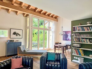 A spacious living room with a large window, a bookshelf, and a dining area. - Maisonette Alpenrose by Interhome (Sils Maria)