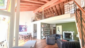 Un vaste espace de vie doté d’un haut plafond, de poutres apparentes, d’une cheminée, d’un coin repas et d’un balcon.