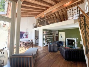 A spacious living area with a high ceiling, a fireplace, a bookshelf, and a dining area. - Maisonette Alpenrose by Interhome (Sils Maria)