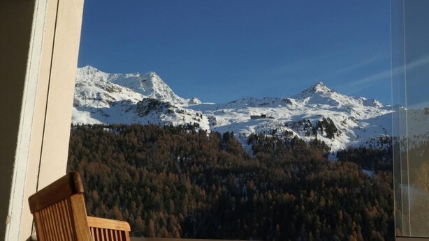 Blick auf Berge vom Balkon mit einem Holzstuhl.