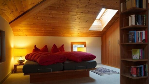 Een gezellig zolderkamer met een hoogslaper, dakraam, bedlampje en een boekenplank.