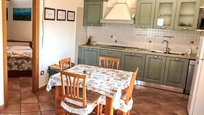 A compact kitchen with green cabinets, a dining table with chairs, and a tiled floor.