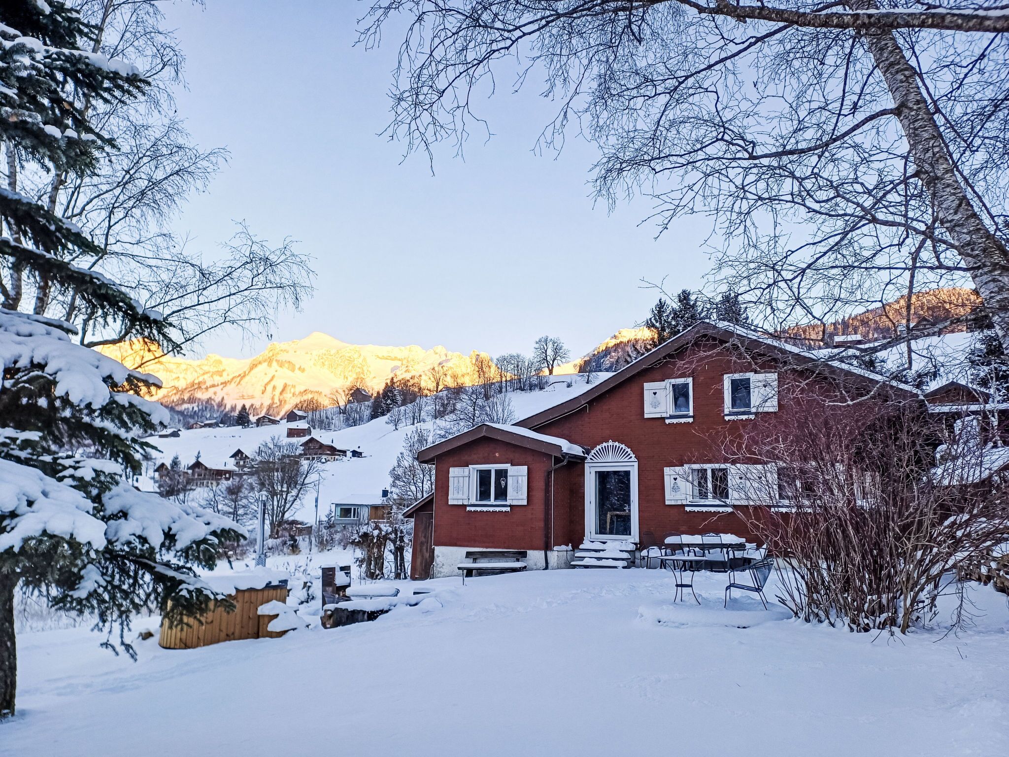 Ein rotes Haus mit einem verschneiten Hof und Bergen im Hintergrund.