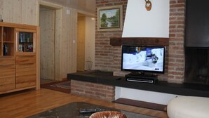 A living room with a TV, a fireplace, a wooden cabinet, and a framed picture on the wall. - Casa Uccello by Interhome (Wildhaus)