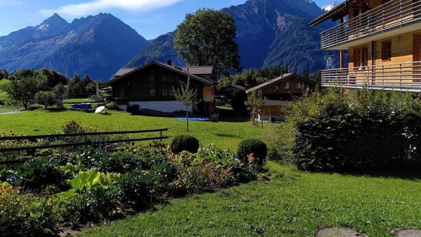 A mountain lodge with a wooden exterior, surrounded by lush greenery and a view of snow-capped mountains. - Engi 484j by Interhome (Hasliberg)