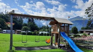 Un parque infantil con columpios, un tobogán y una casita de juegos de madera.