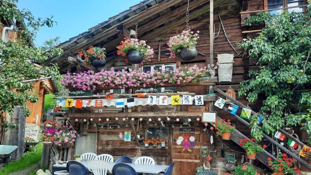 Un edificio de madera rústica con un balcón decorado con macetas colgantes y varias banderas.